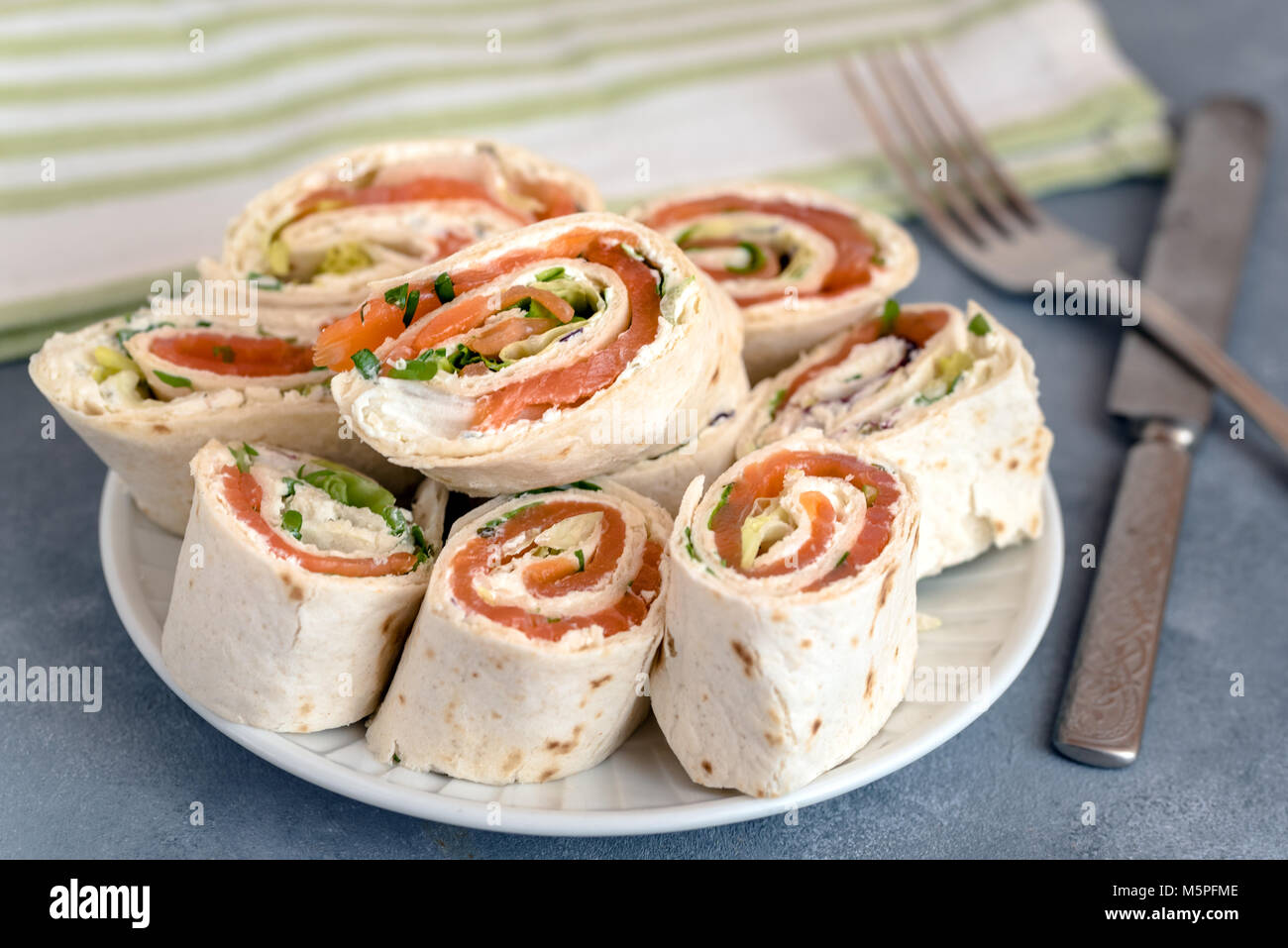 Rolls of thin pancakes with smoked salmon, cream cheese, chives and lettuce. Stock Photo