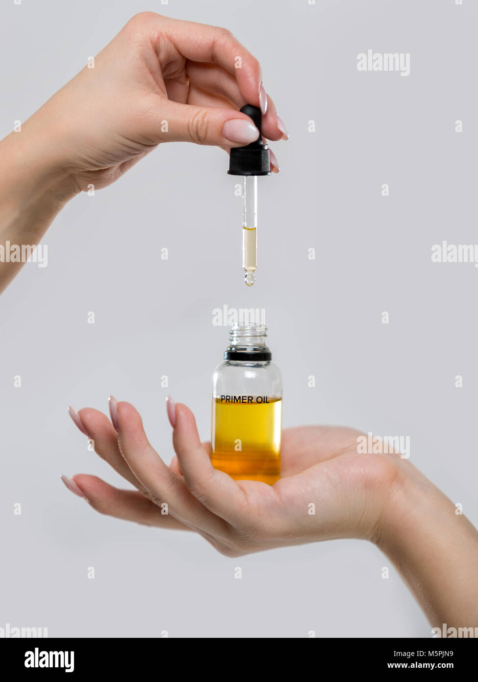 Bottle of oil for the face in women's hands. Photo of a primer close-up on a gray background Stock Photo