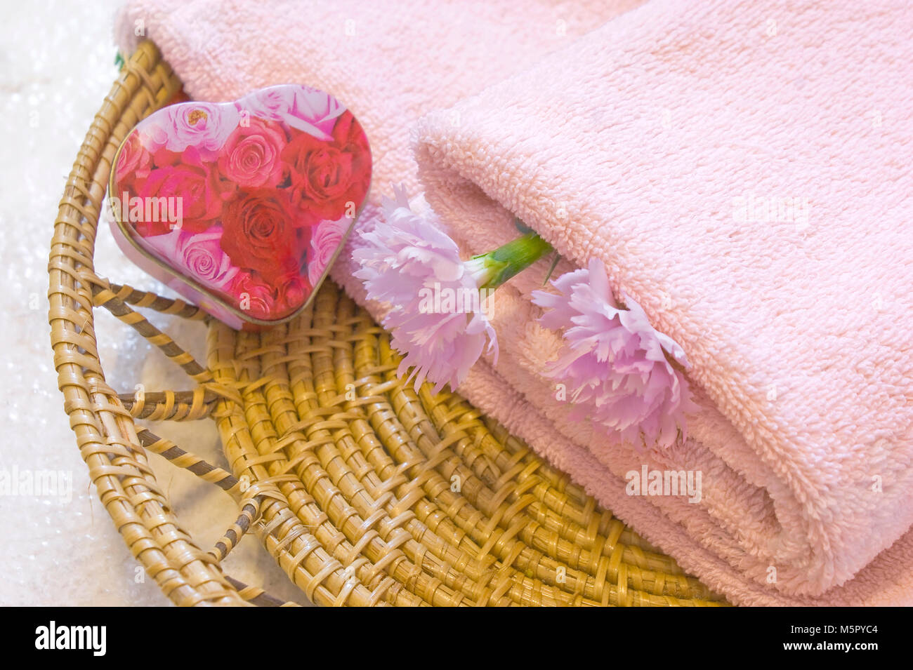 Towel, container with soap in the form of a heart in the braided plate with two carnation flowers Stock Photo