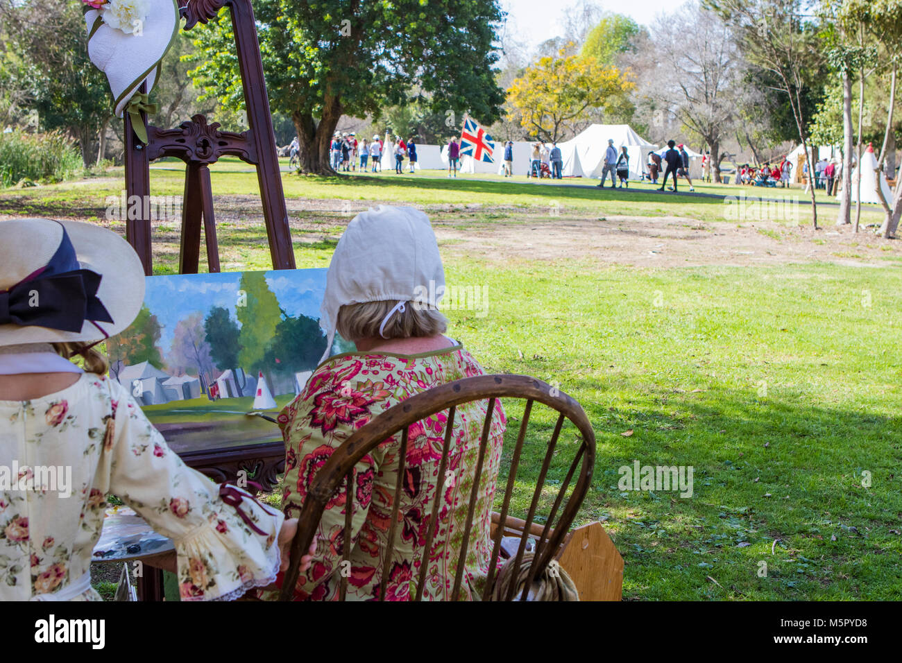 Female artist seated on a chair painting a British Army encampment at a American revolution battle reenactment in Huntington Beach California USA Stock Photo