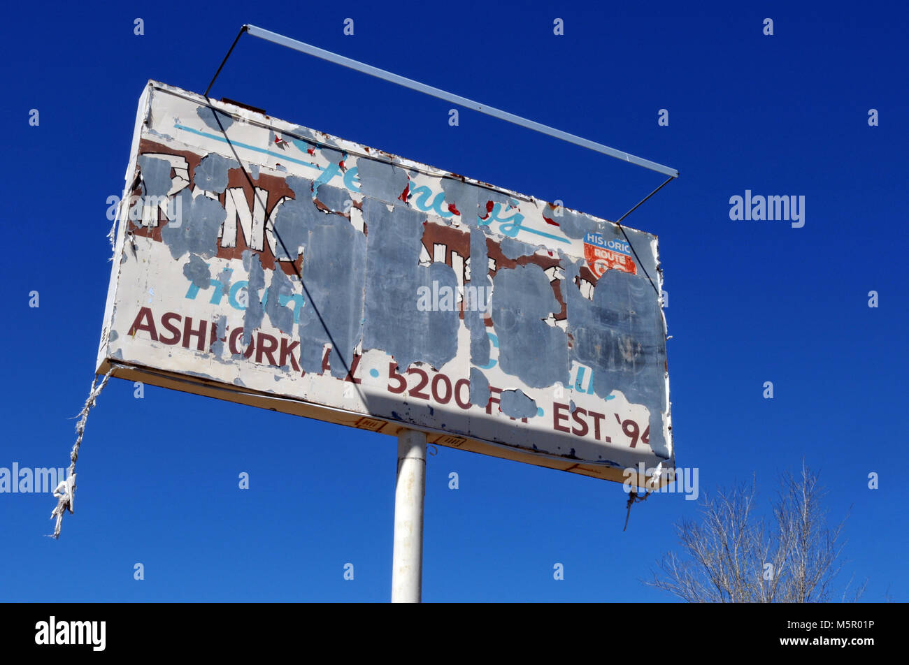 A tattered billboard stands in the Route 66 town of Ash Fork, Arizona against a bright blue sky. Stock Photo