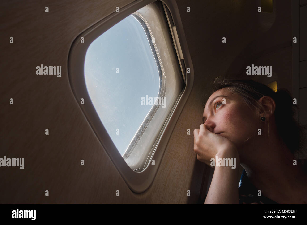 Sad woman at porthole in plane Stock Photo