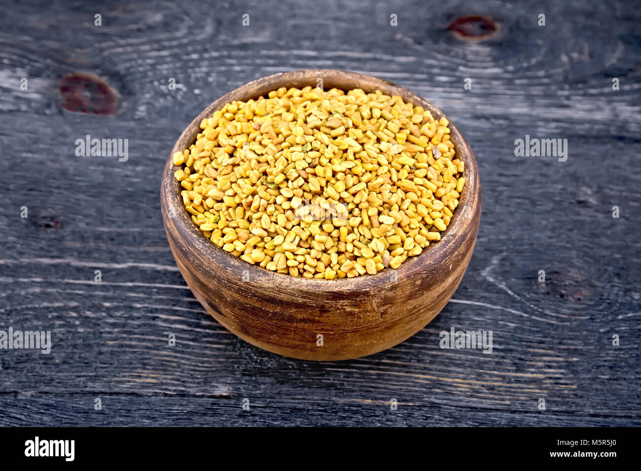 Fenugreek seeds in a clay bowl on the background of a wooden board Stock Photo