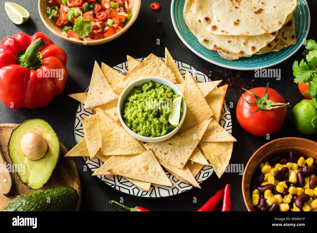 Mexican food Guacamole Nachos Tortilla chips salsa and beans on dark