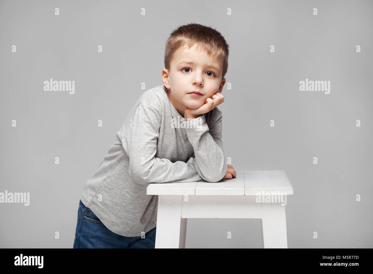 Portrait of a cute boy with standing at the chair in the photostudio on grey background Stock Photo