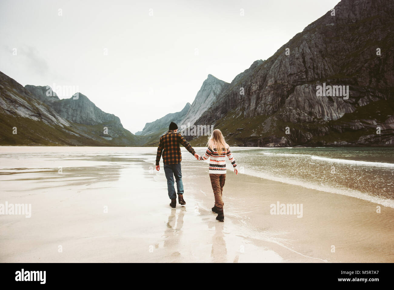 Romantic Couple in love walking holding hands on sea beach in Norway man and woman together traveling Lifestyle concept vacations outdoor Stock Photo