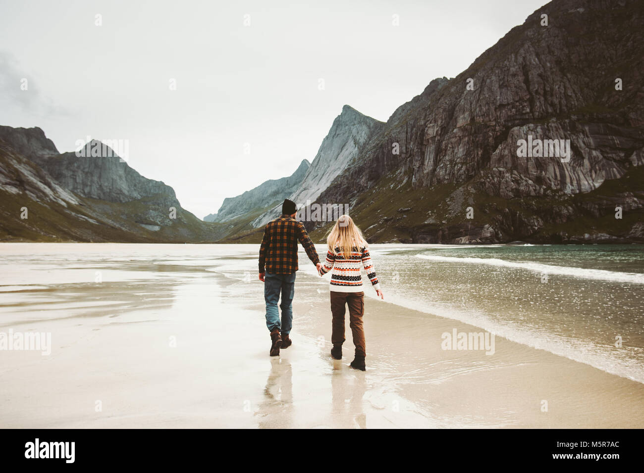 Couple in love walking holding hands on wild sea beach in Norway Man and Woman together traveling Lifestyle concept romantic vacations Stock Photo