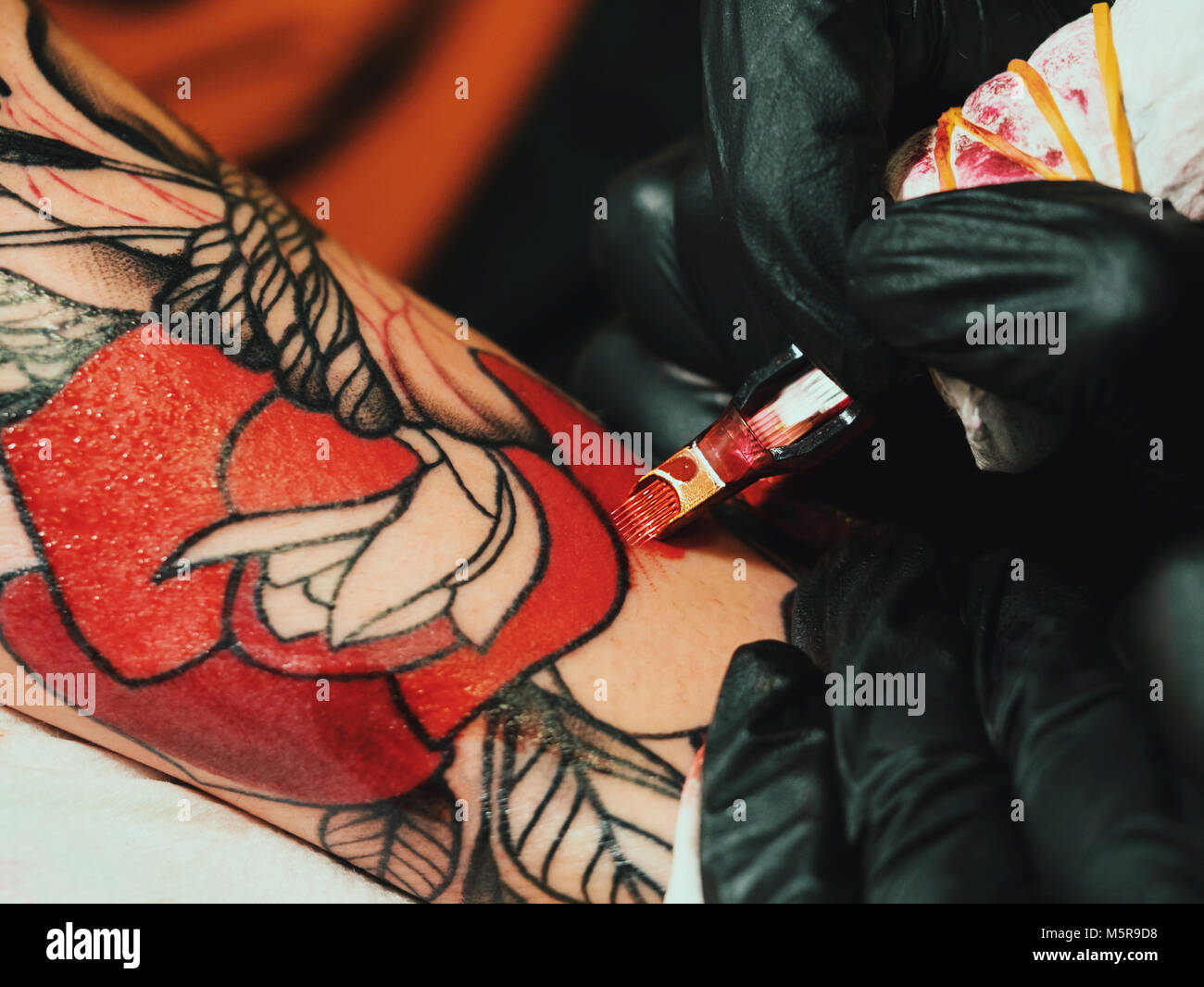 Tattoo artist at work. Woman in black latex glove tattooing a young man