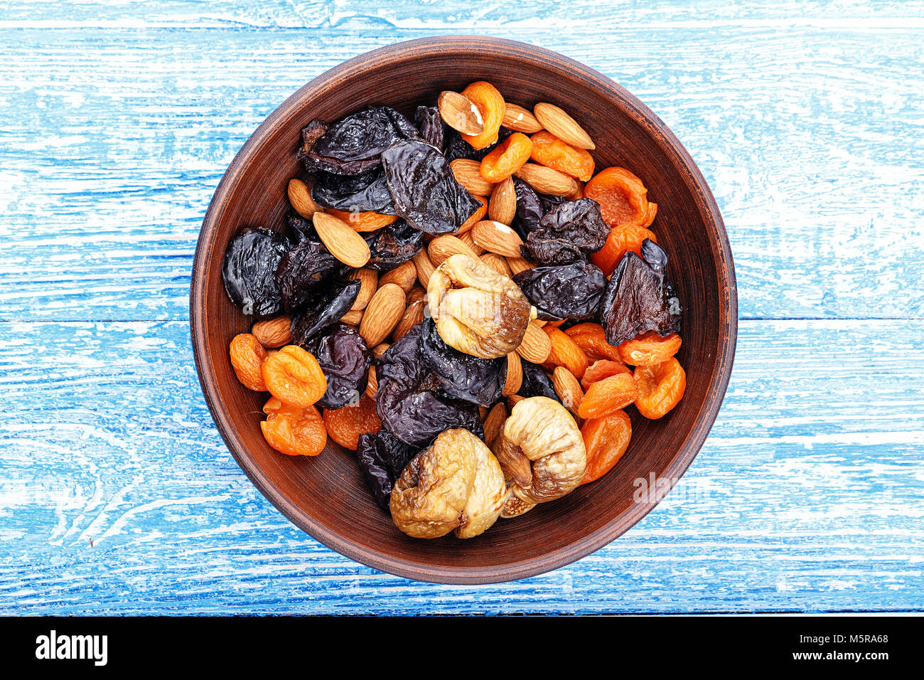 Dried figs, dried apricots and prunes in a mix with almonds in a clay plate  on a wooden table, horizontal photo Stock Photo - Alamy