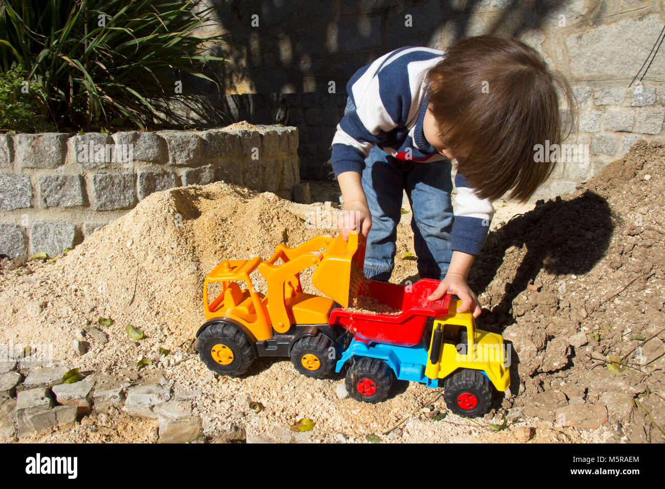 little three year old boy playing in the sand with a digger and dump truck. Stock Photo