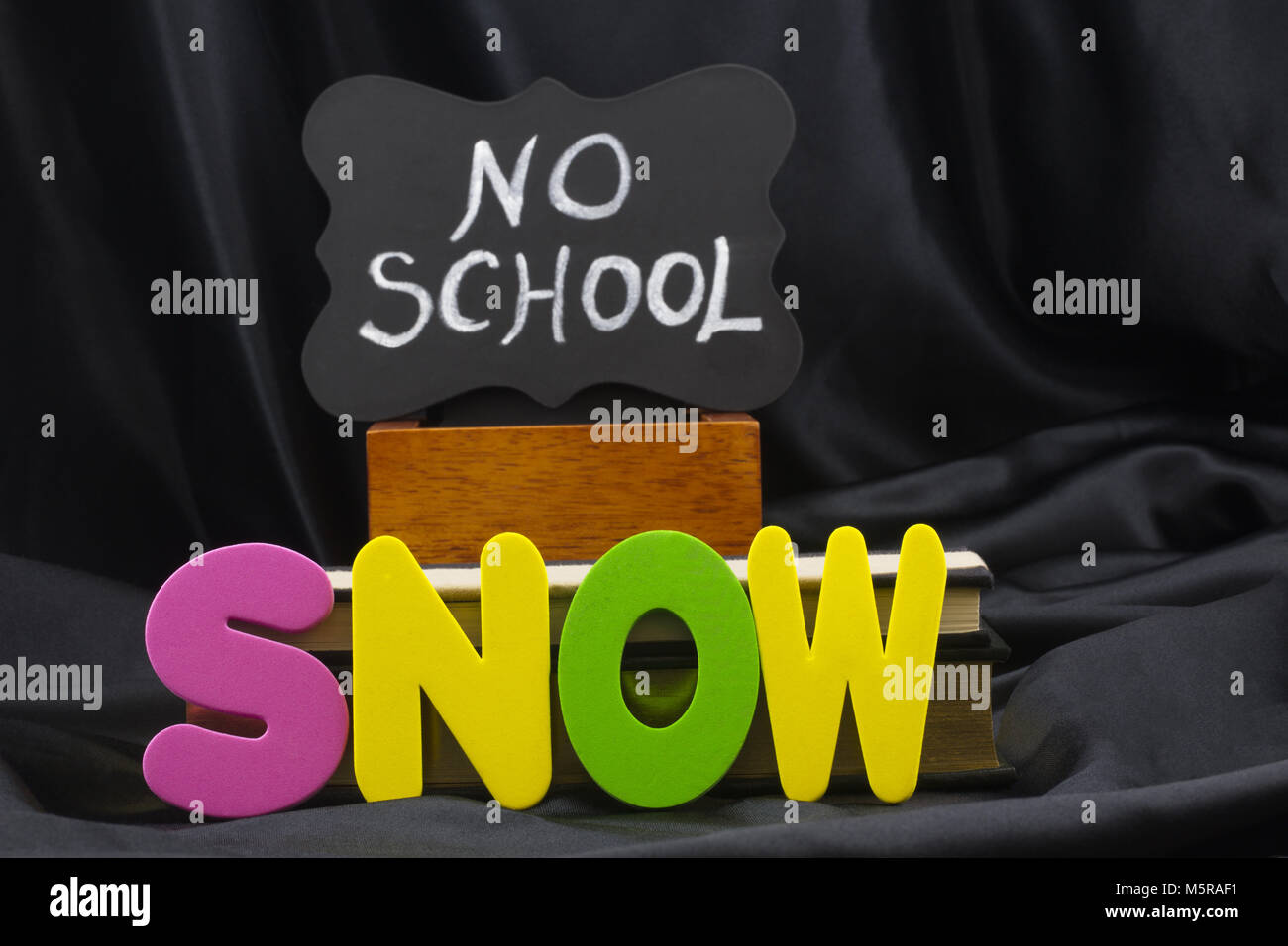 SNOW letters in front of a chalkboard NO SCHOOL sign reflects a winter weather safety closing for area schools.  Letters and signage with black backgr Stock Photo