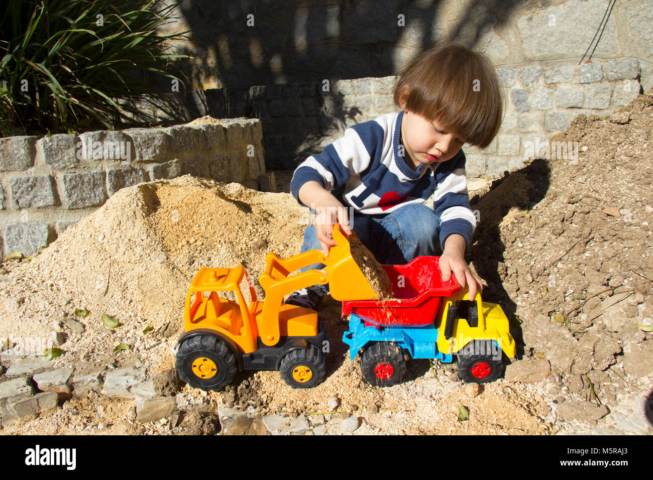 little three year old boy playing in the sand with a digger and dump ...