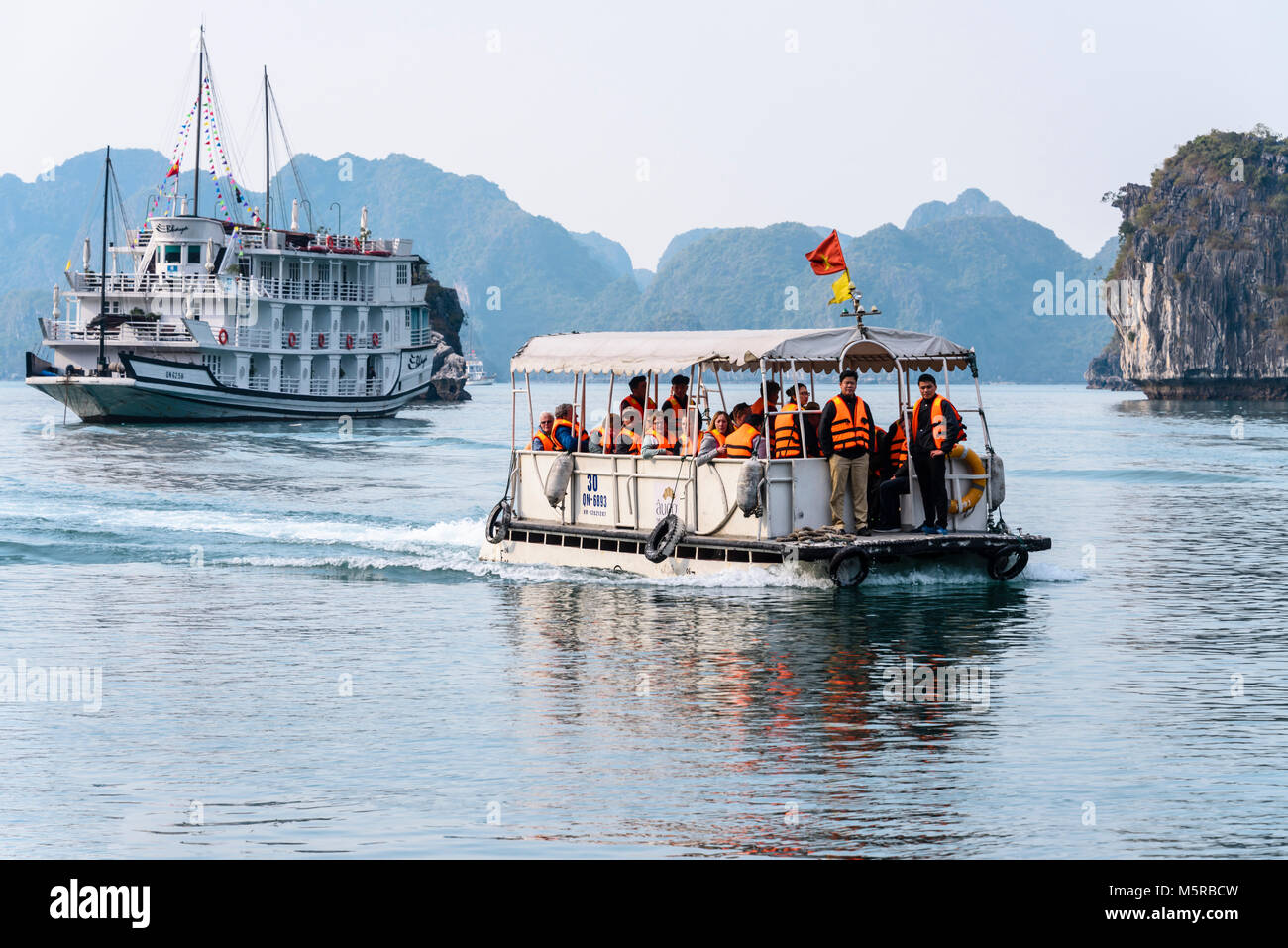 Tourists wearing orange life jackets are taken from their cruise ship in a tender to the Cua Van floating village, Halong Bay, Vietnam Stock Photo