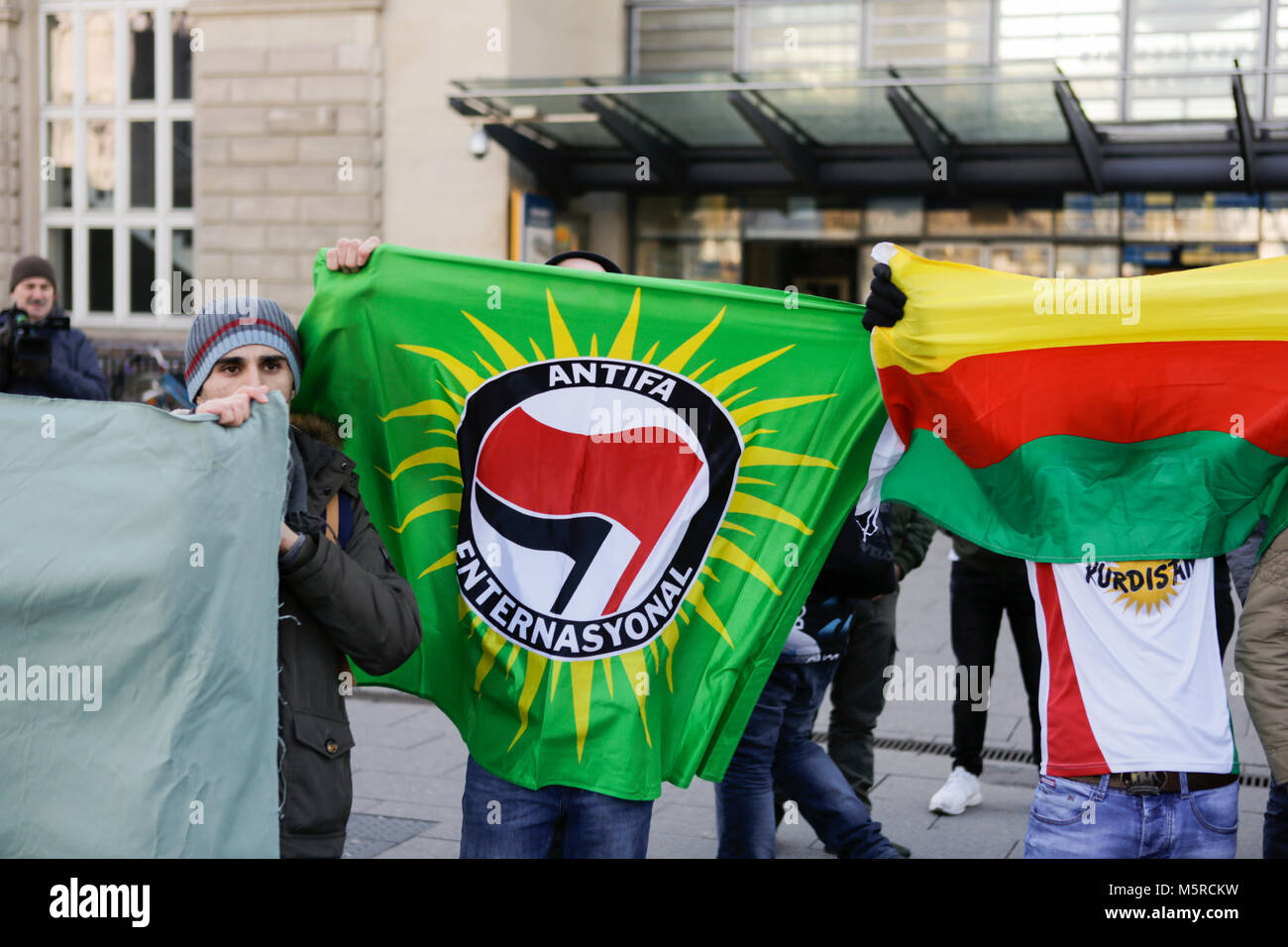Mannheim, Germany. 25th Feb, 2018. Kurdish protesters holds up a flag of  Antifa Enternasyonal and a flag of Rojava. Turkish and Kurdish protesters  faced each others at protests in the city centre