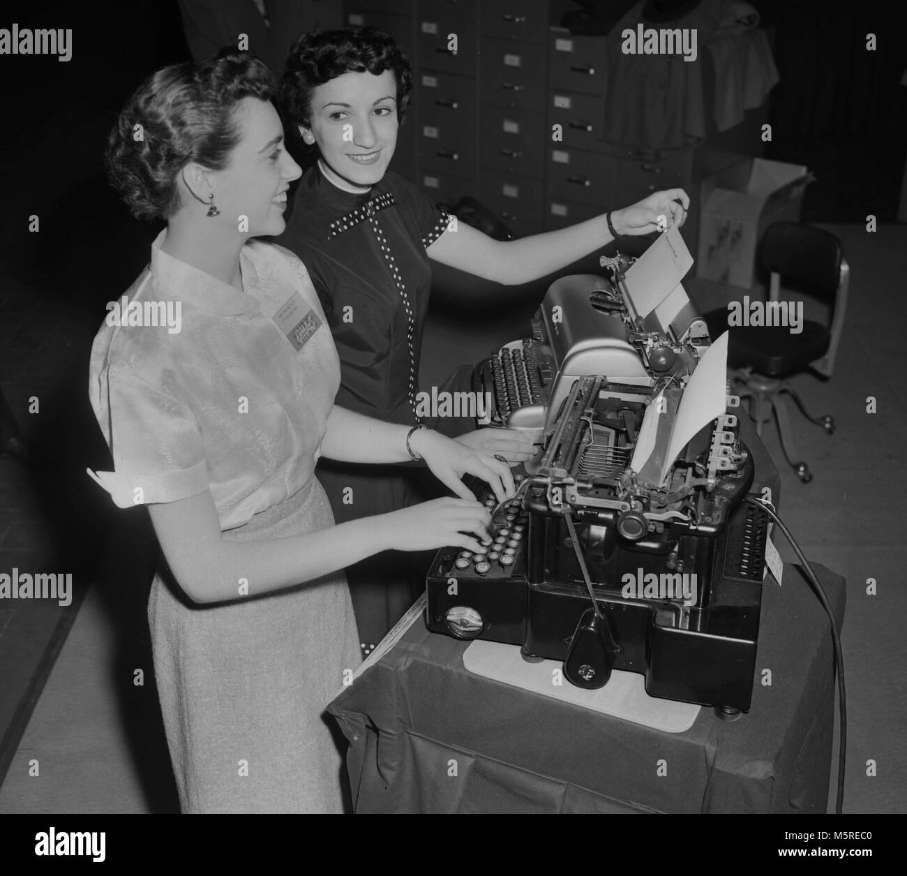 Two models demonstrate Remington electric typewriters at an office equipment convention in Chicago, ca. 1955.  The typewriter in back is the modern 1955 model and the very first Remington electric is in the front from 1925. Stock Photo