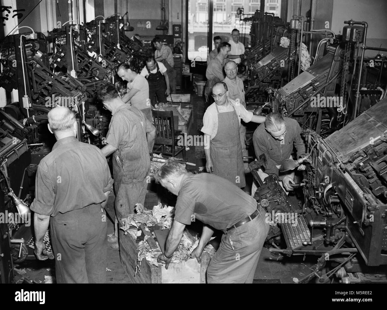 Workers assemble and configure linotype printing presses for a newspaper printing operation in Chicago, ca. 1949. Stock Photo