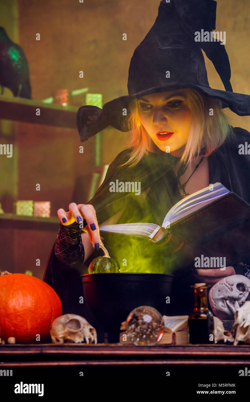 Picture of witch blonde in black hat with book brewing potion in pot Stock Photo Alamy
