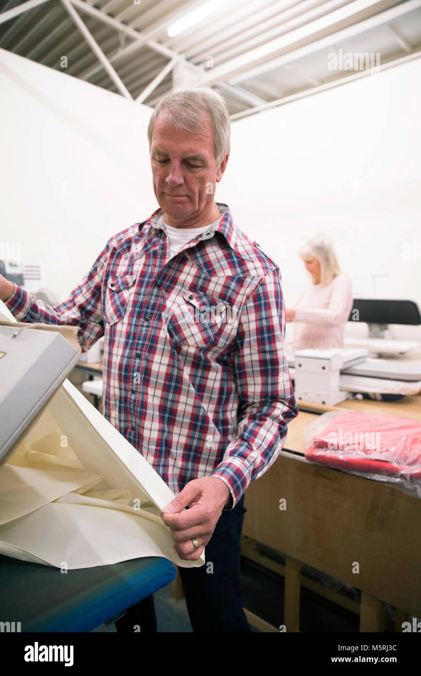 Senior man is pressing fabric in a business warehouse. Stock Photo