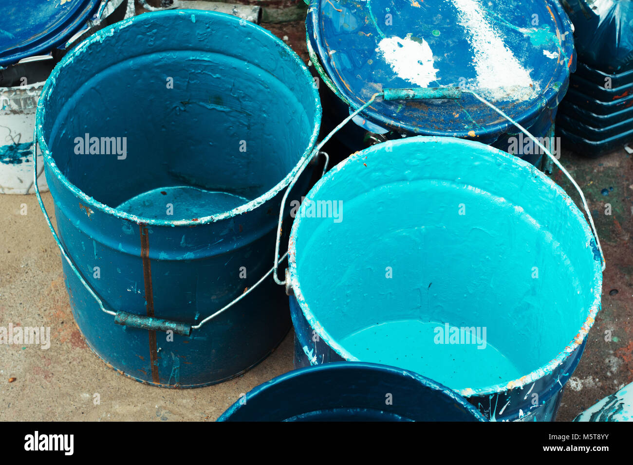 Paint dirty bucket with blue color on asphalt with paintbrush.Old paint