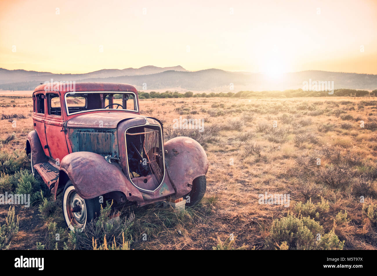 Old rusty antique car, abandoned in a field at sunset Stock Photo