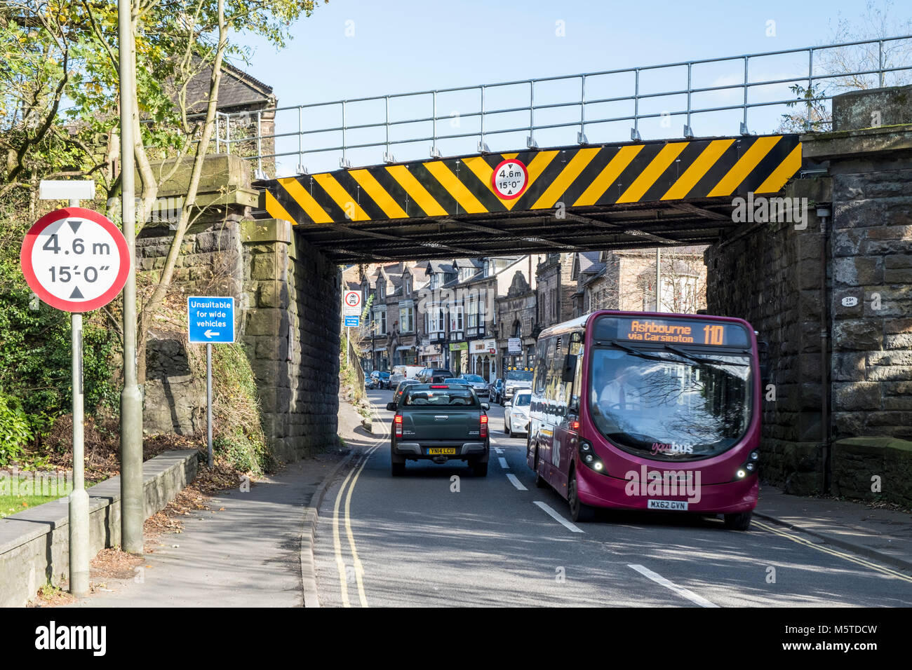 Bus travelling under a low bridge on a road, Matlock, Derbyshire