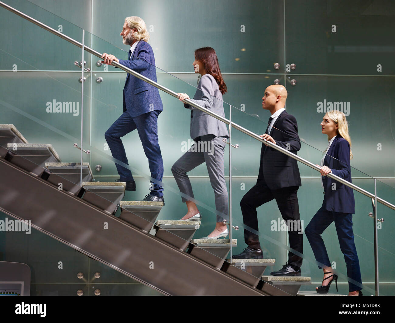 multinational and multiethnic corporate business people male and female walking up stairs in a line in modern office building. Stock Photo
