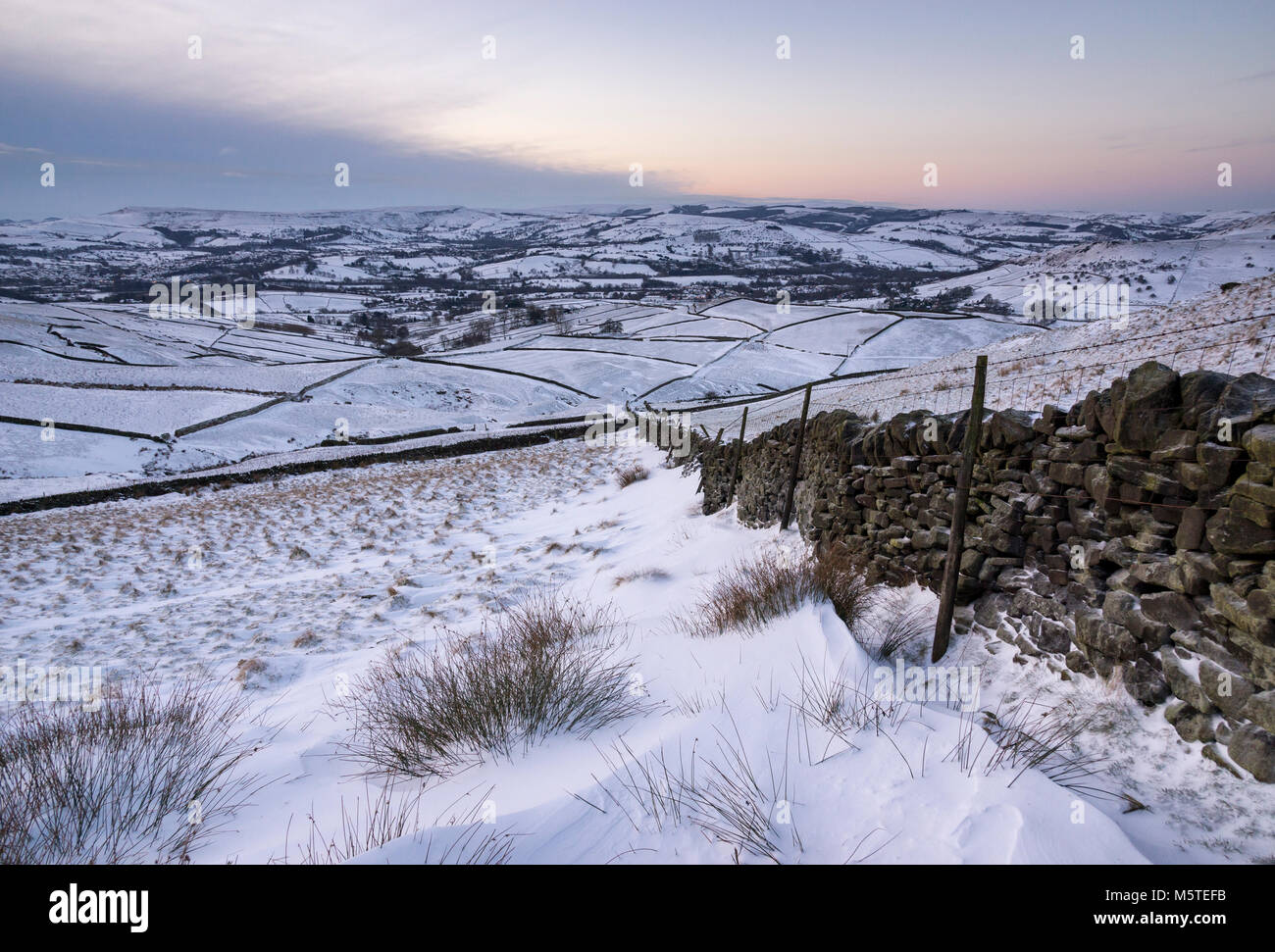 Snowy winter morning in the hills of the Peak District. Snowdrifts against a drystone wall. View to Chapel-en-le-frith in Derbyshire, England. Stock Photo