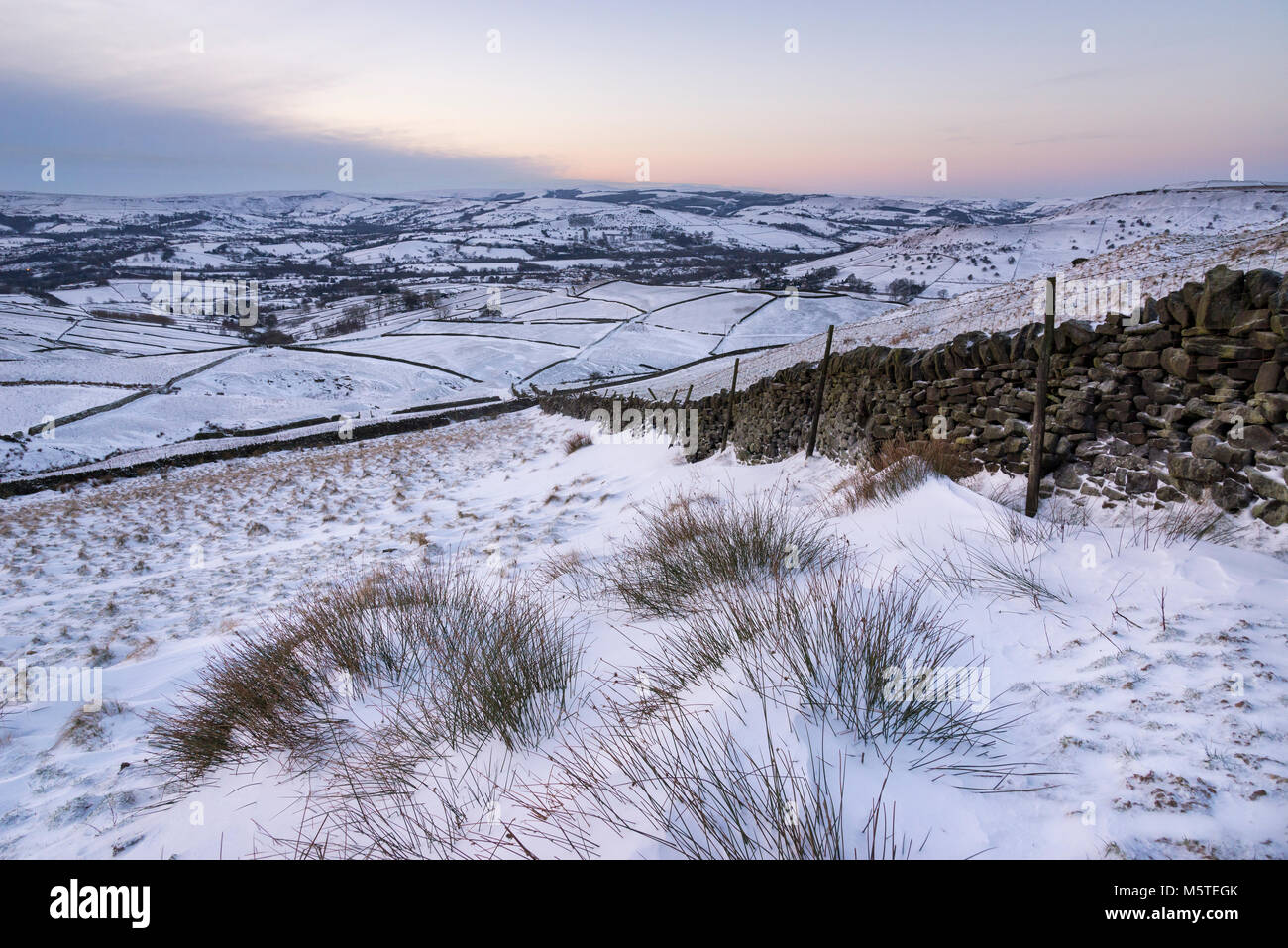 Snowy winter morning in the hills of the Peak District. Snowdrifts against a drystone wall. View to Chapel-en-le-frith in Derbyshire, England. Stock Photo