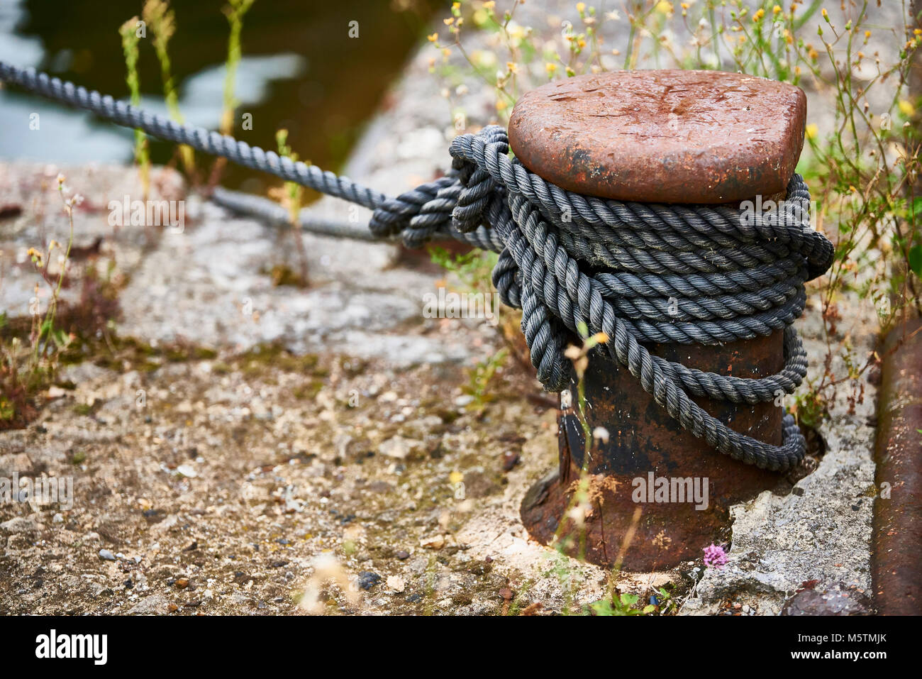 Old rusty iron bollard with tied rope Stock Photo