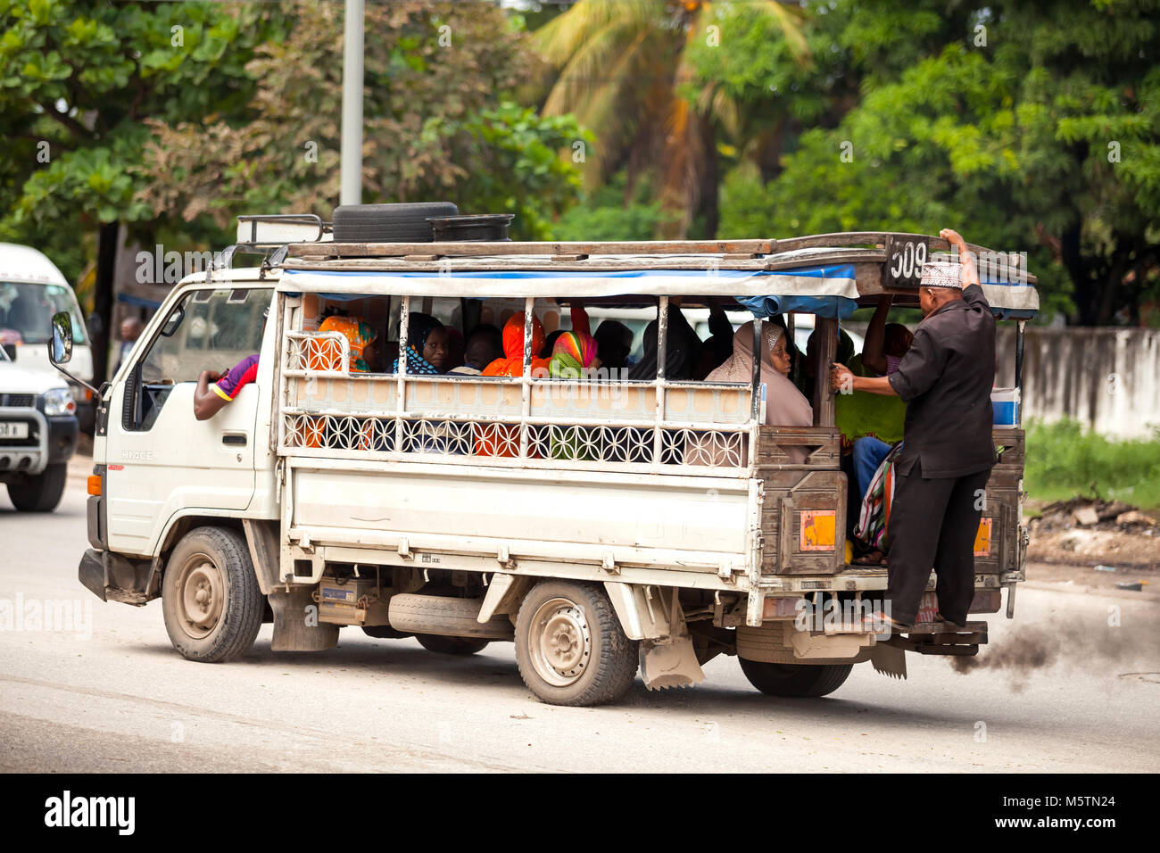 Taxi taking people to market. Man riding on back of taxi. Stock Photo