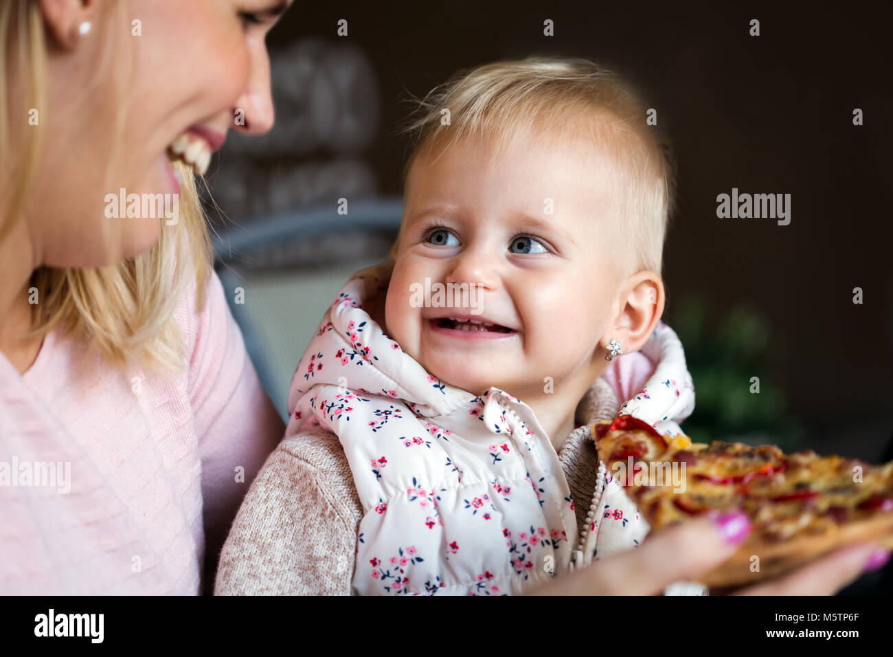 Little girl eats a large slice of pizza from her mother's hands. Children's pizza. Stock Photo