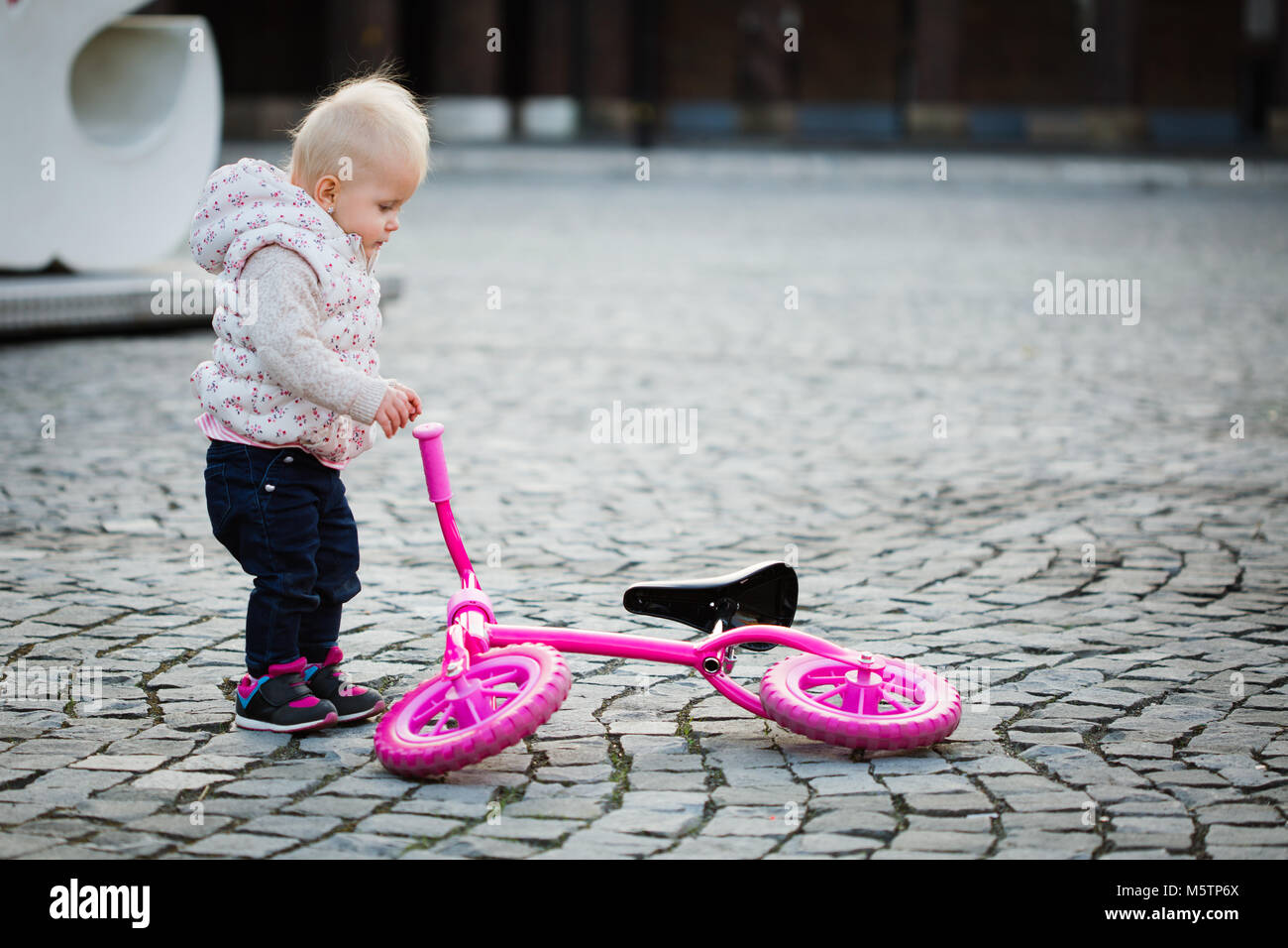 Focused little girl to ride balance bike outdoors, cute small baby trying bicycle Stock Photo