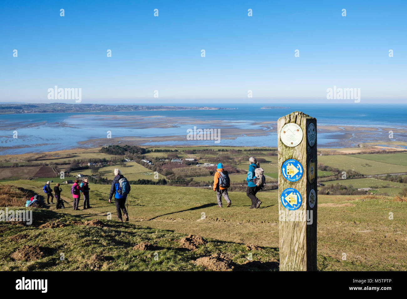 Circular Route footpath sign on North Wales Path with hikers hiking and view to Menai Strait on coast. Abergwyngregyn, Gwynedd, Wales, UK, Britain Stock Photo