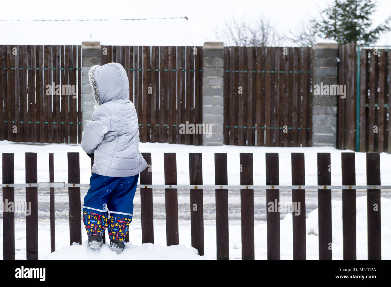 Child looking over the fence. Authentic lifestyle winter garden scene with unrecognisable kid. Stock Photo