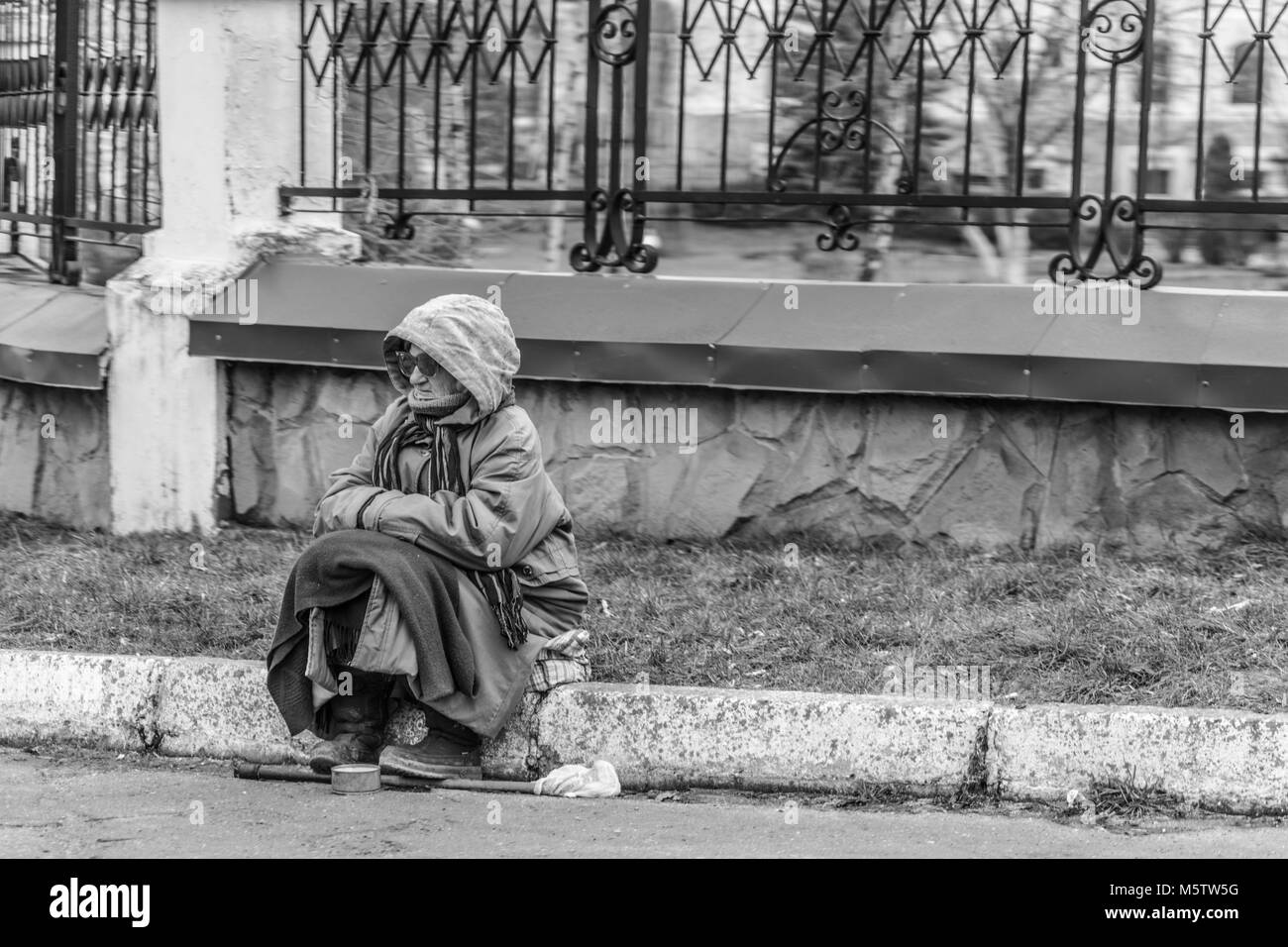 A woman sits on the road near the park and asks for money. Black and white photo. Stock Photo