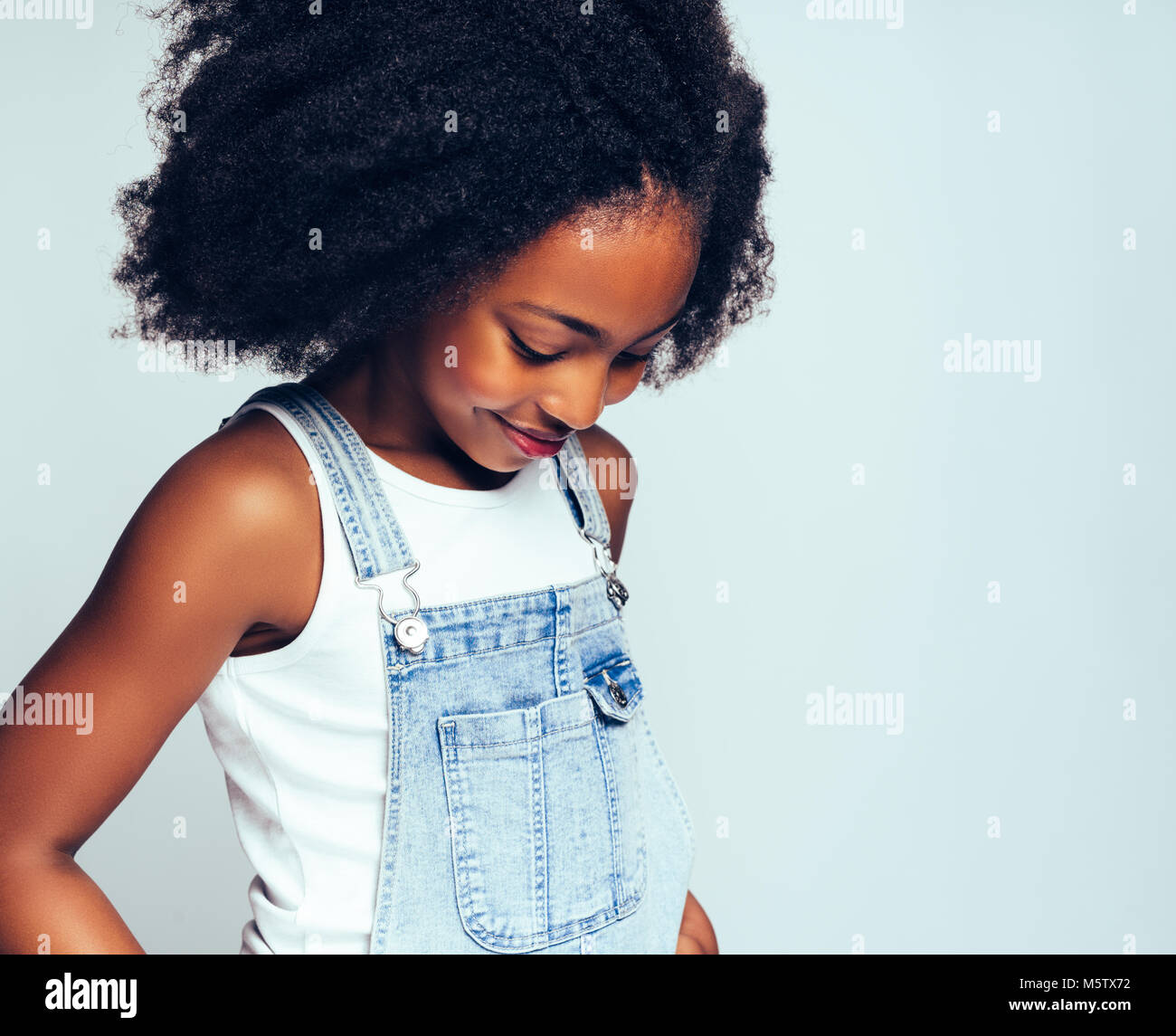 Young African girl with long curly hair and wearing dungarees smiling ...