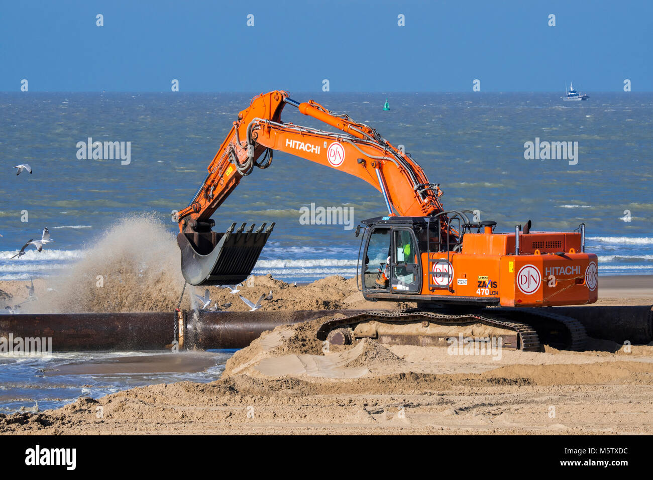 Hydraulic excavator connecting pipes of pipeline during sand