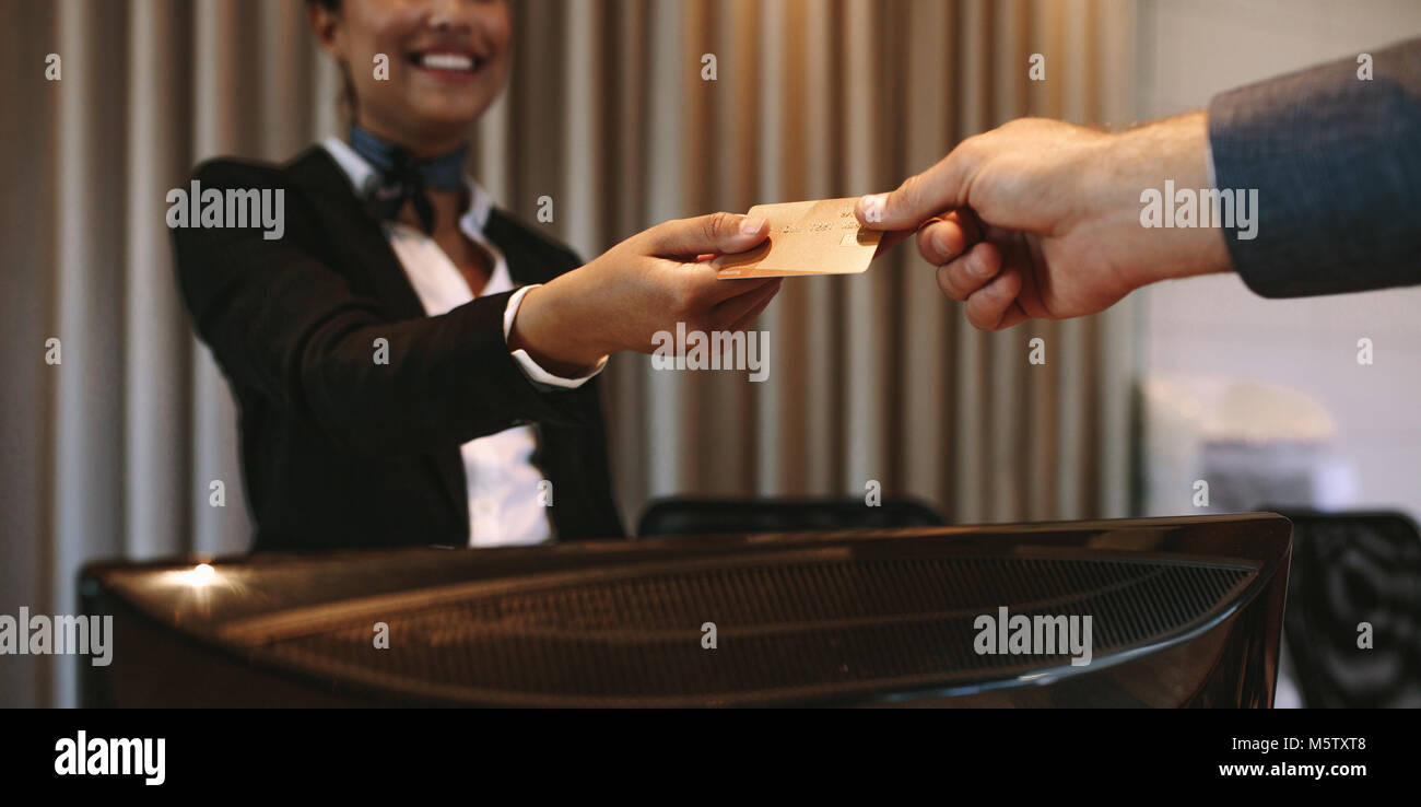 Close up of businessman paying with credit card at reception desk in hotel. Business man giving credit card to hotel receptionist for payment of his r Stock Photo