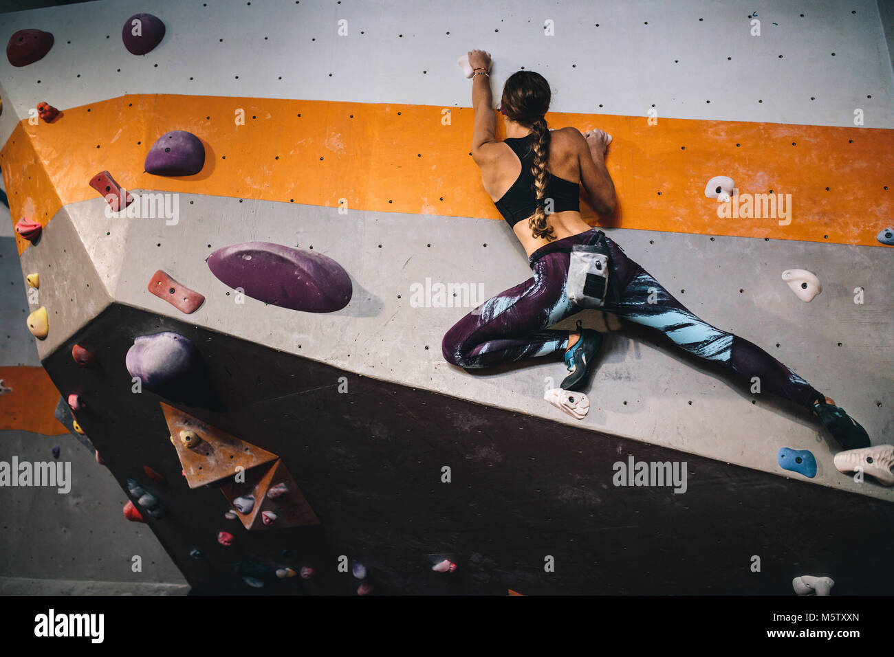 Athletic woman bouldering at an indoor climbing centre. Professional