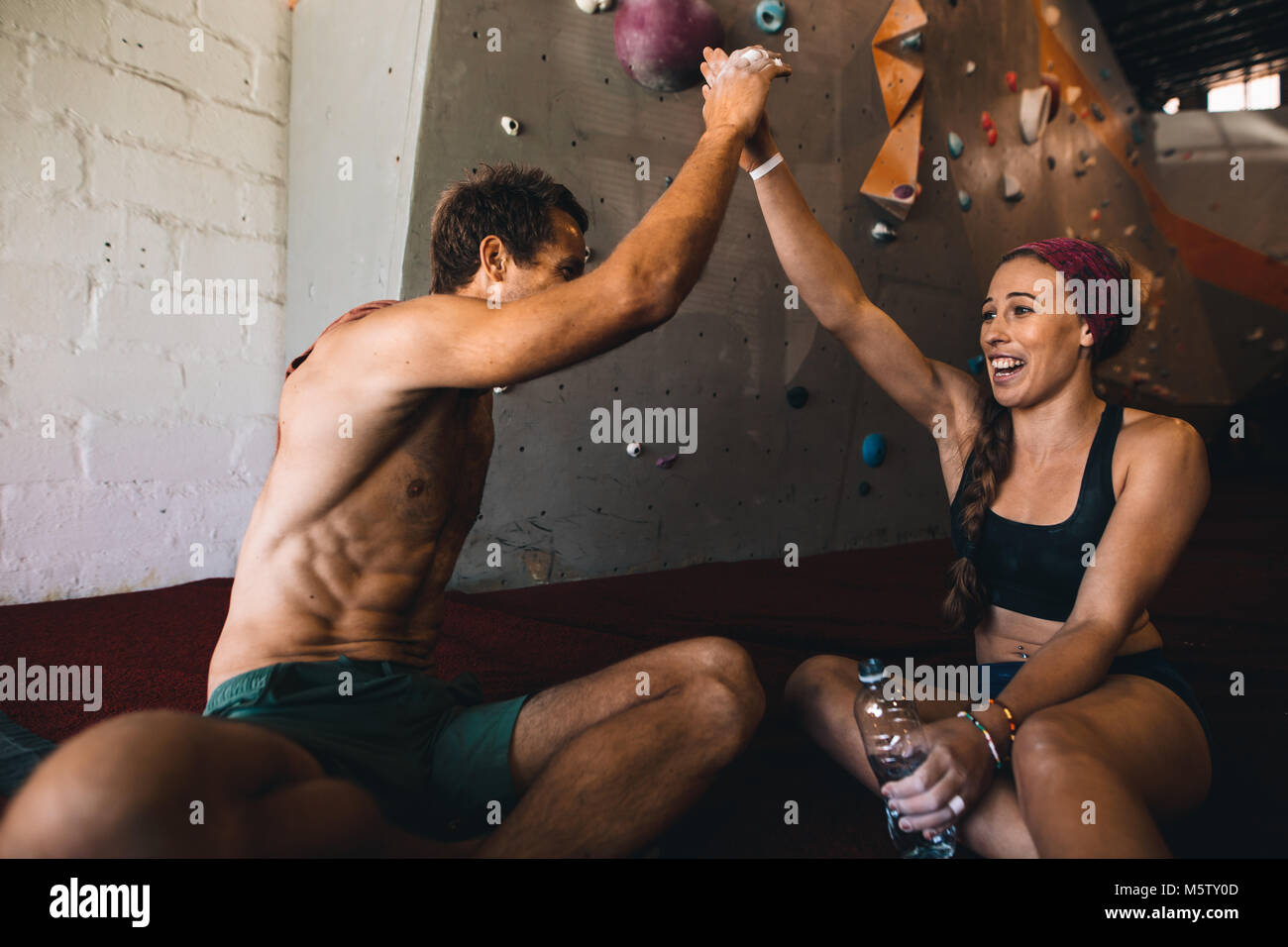 Man and woman rock climbers giving high five after successfully completing wall climbing. Happy rock climbing couple relaxing after work out. Stock Photo