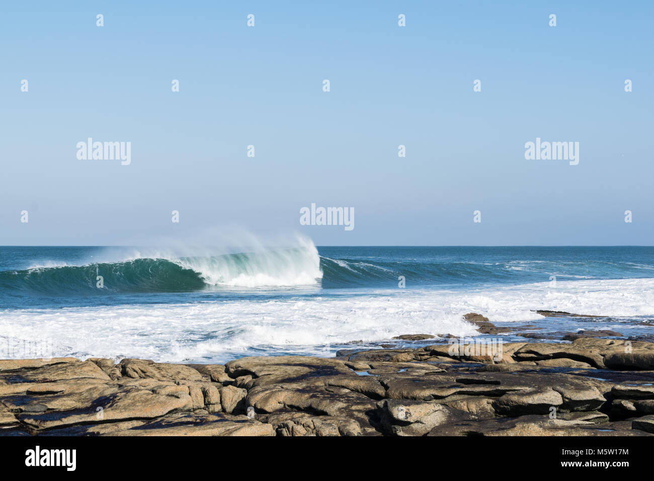 Waves crashing on to a rocky beach on a clear sunny day Stock Photo