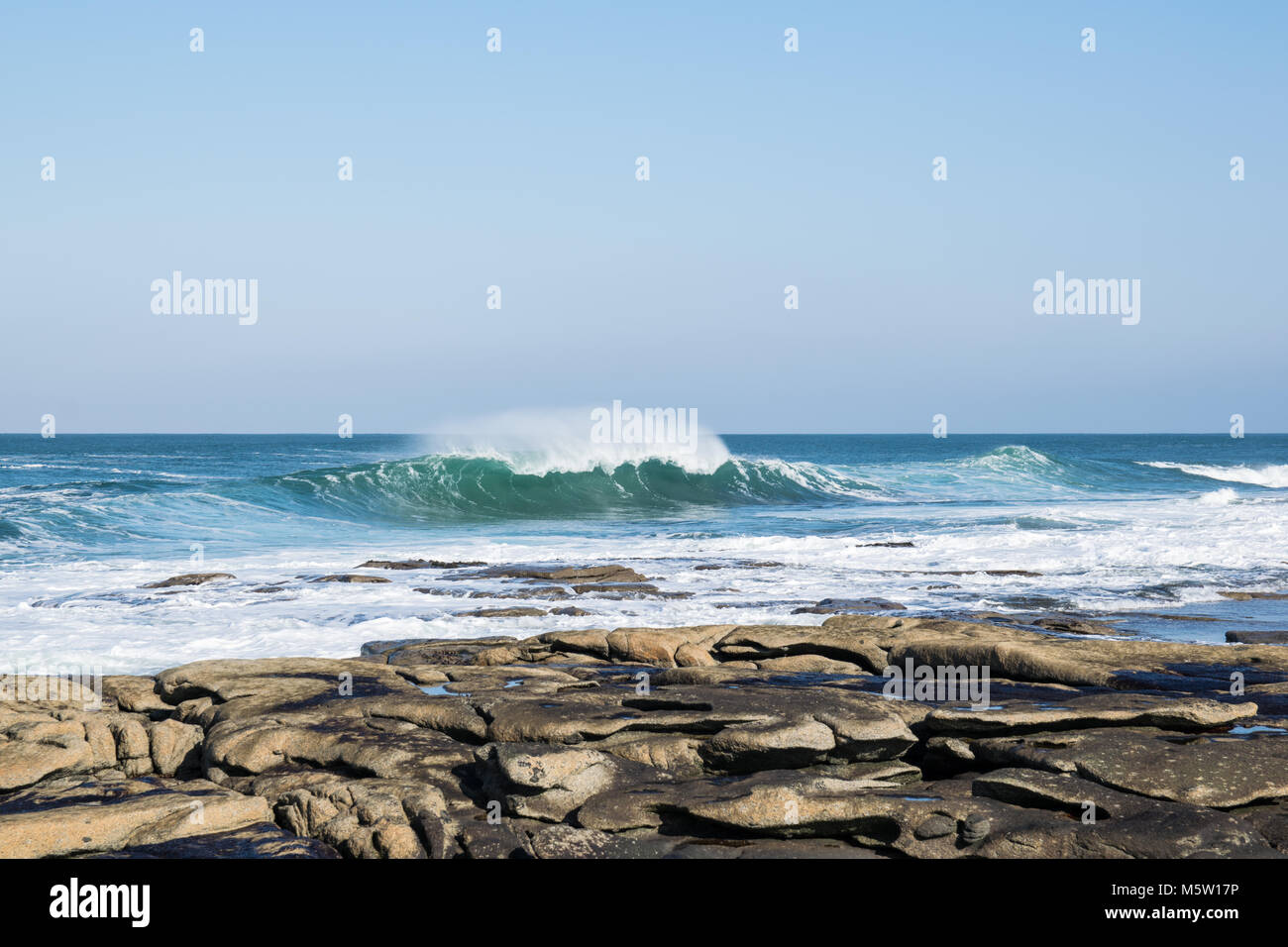 Waves crashing on to a rocky beach on a clear sunny day Stock Photo