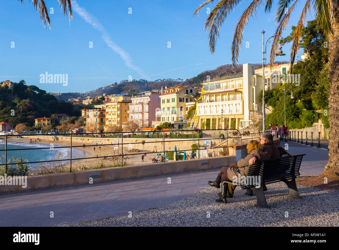 Family of three sitting on a bench admiring the beach view of the famous sea resort tourist town of Lerici, Cinque terre, Liguria, Italy Stock Photo