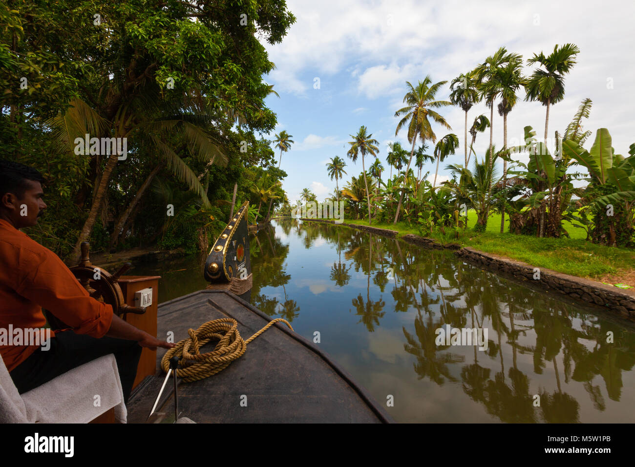The helmsman steering a houseboat on the backwaters near Alleppey and Kumarakom in Kerala, India. Stock Photo
