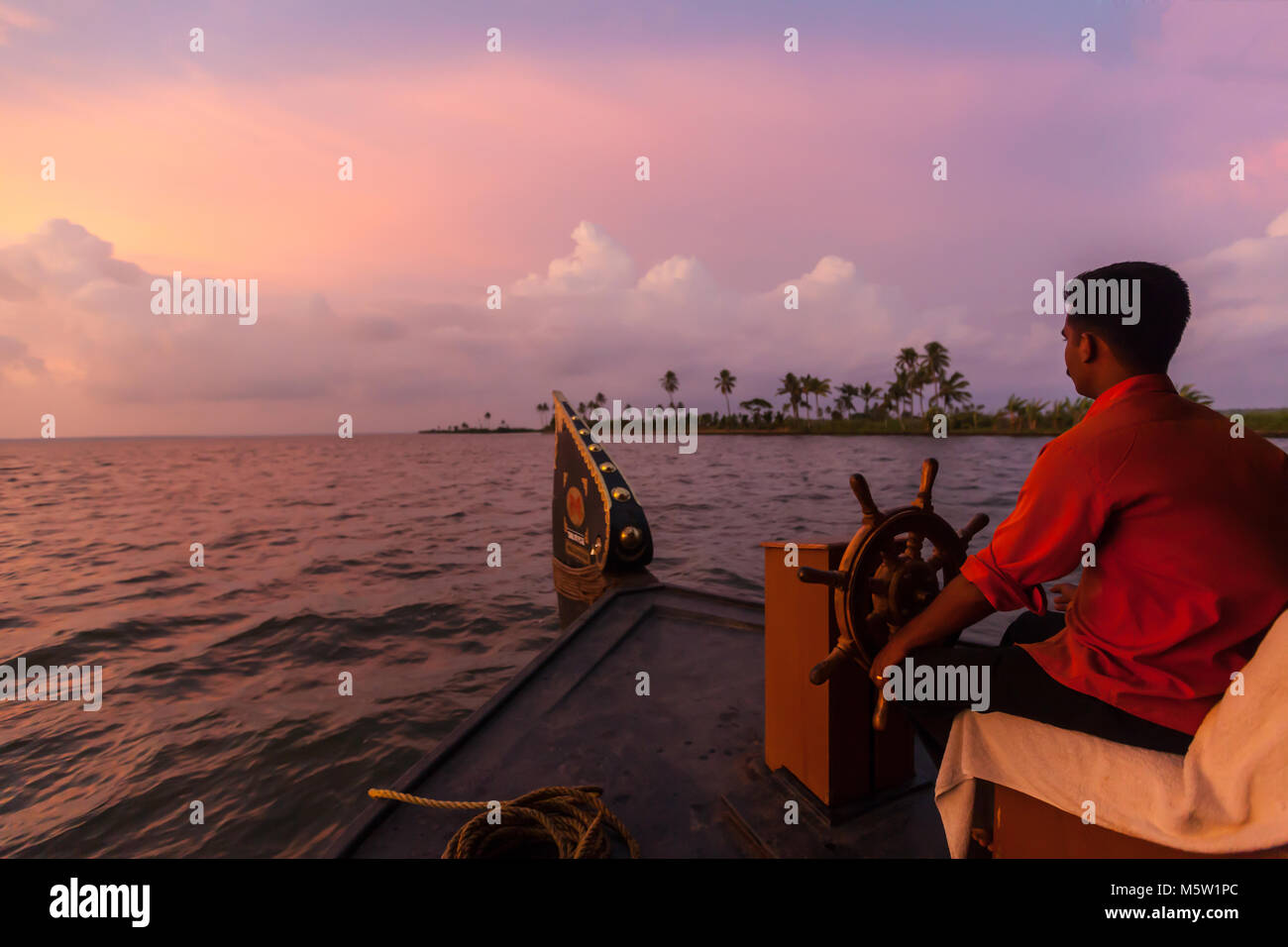 The helmsman steering a houseboat on the backwaters near Alleppey and Kumarakom in Kerala, India. Stock Photo