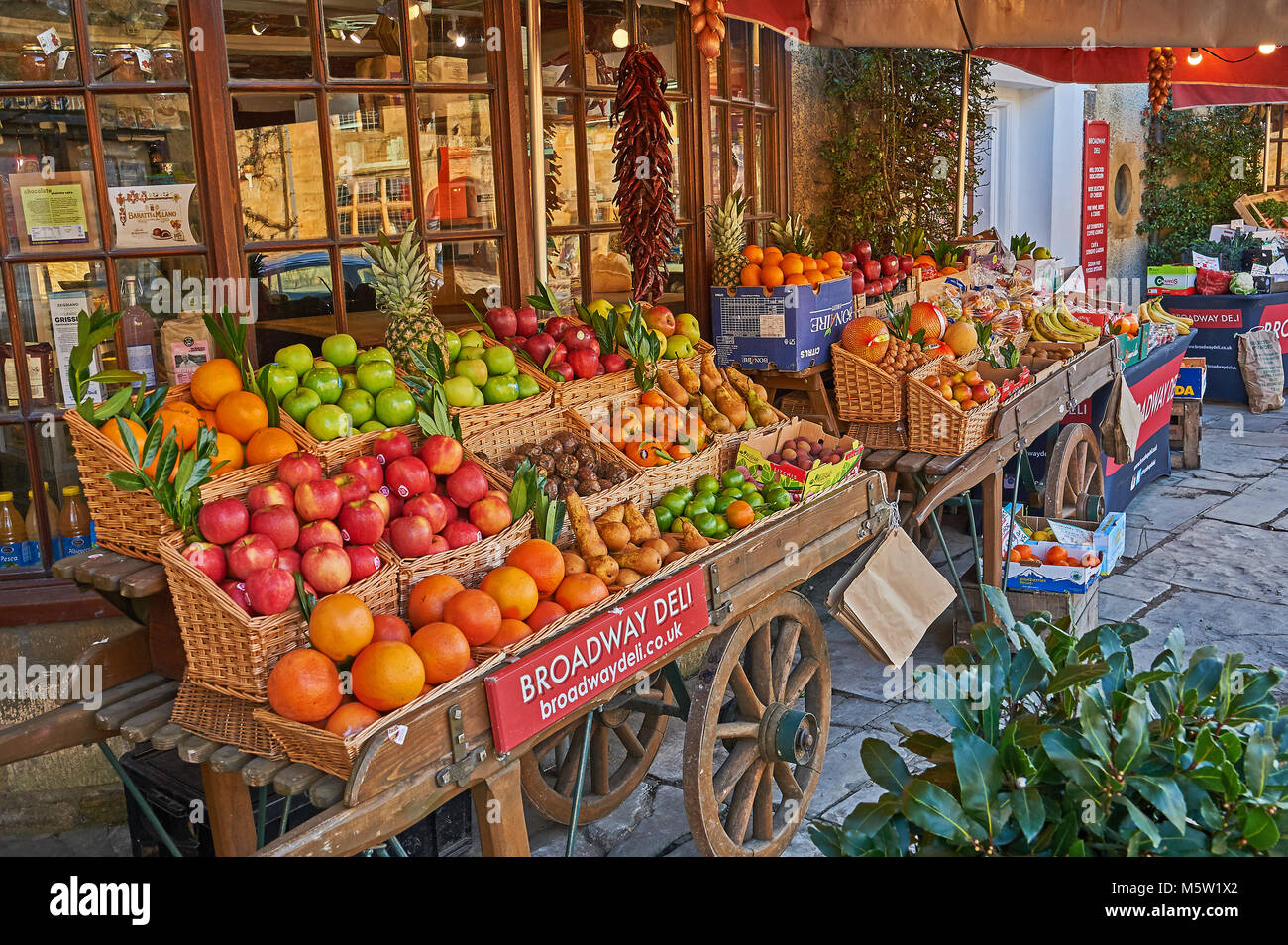 Old fashioned fruit and veg barrow displaying a wide range of fresh fruit and vegetables outside the local deli store in Broadway, Worcestershire Stock Photo