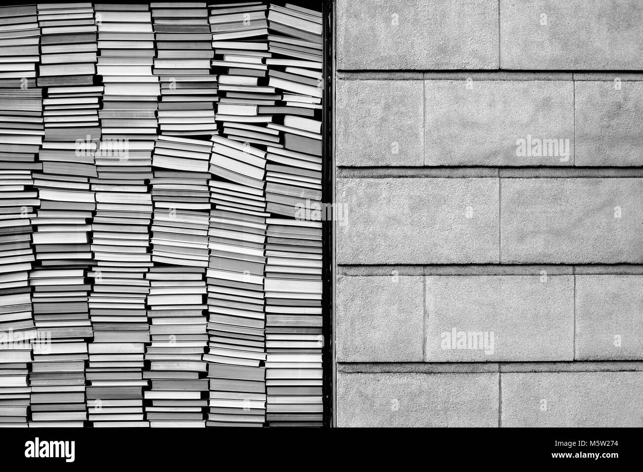 Books stacked against window with brick wall beside them Stock Photo