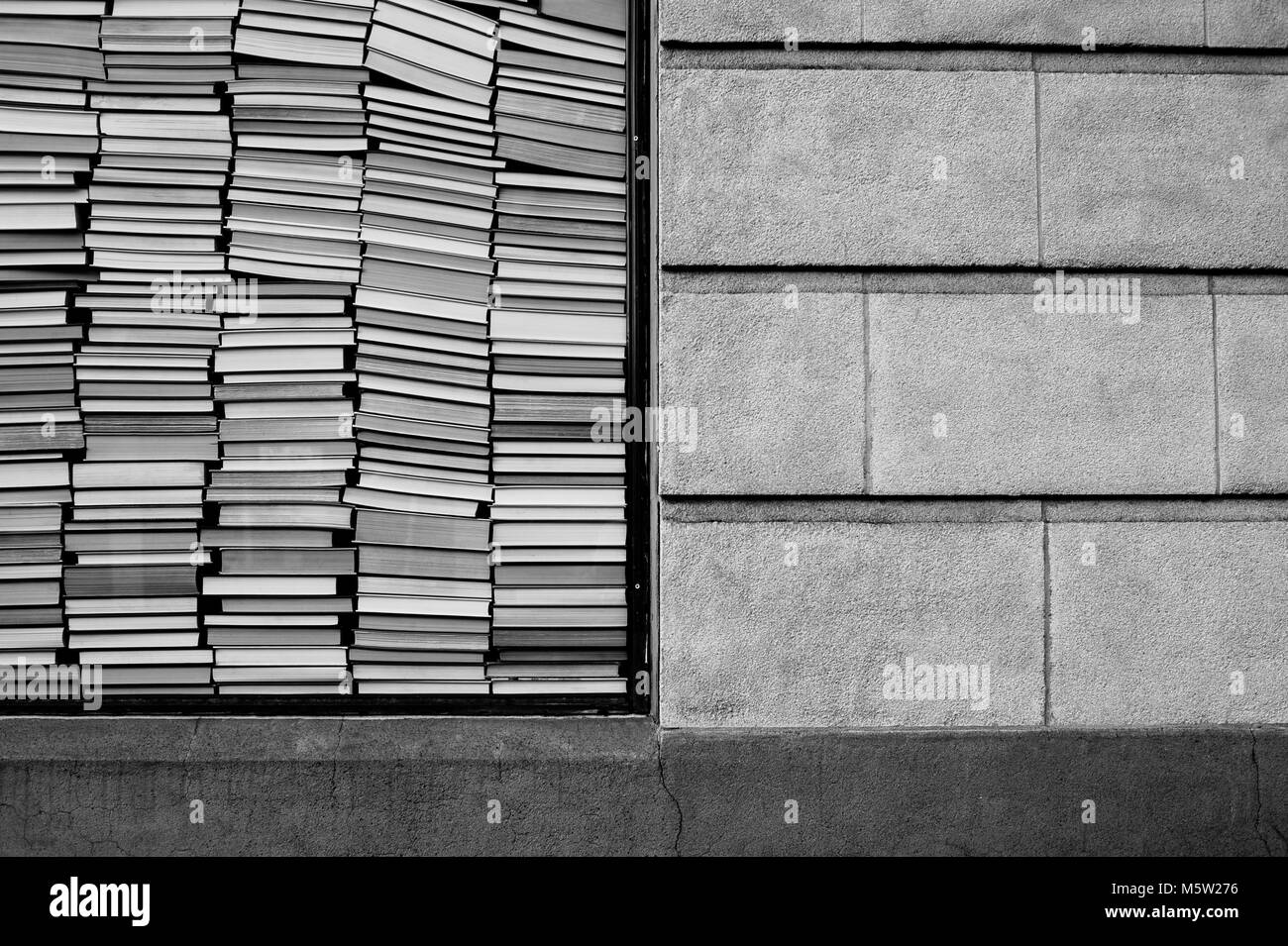 Books stacked against window with brick wall beside them Stock Photo