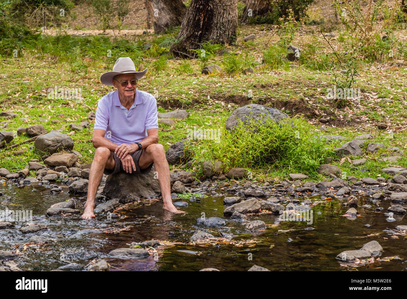 Elderly Australian man, wearing a stetson, sitting by a creek in the Upper Hunter Valley, NSW, Australia. Stock Photo