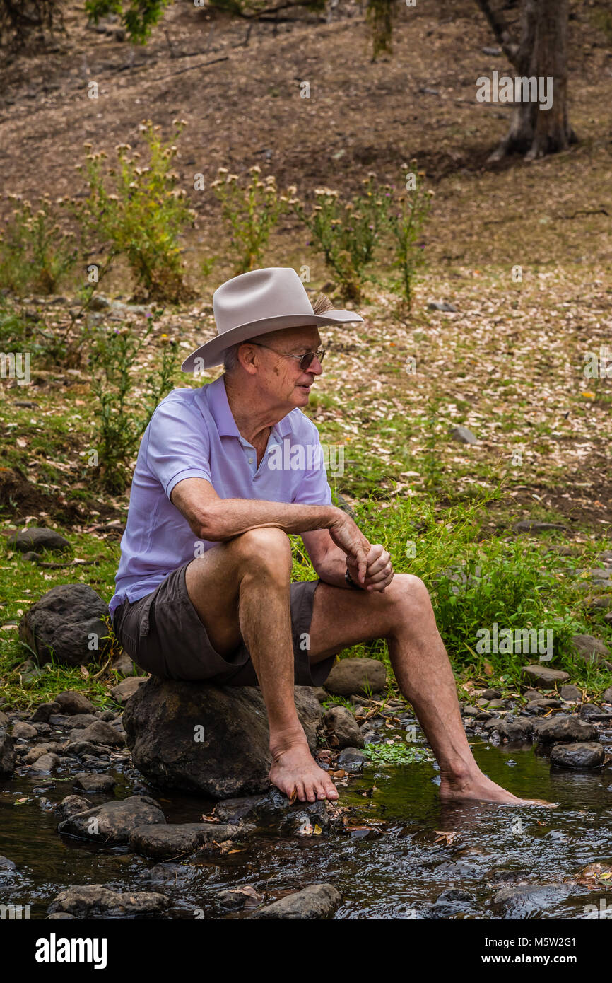 Elderly Australian man, wearing a stetson, sitting by a creek in the upper Hunter Valley, NSW, Australia. Stock Photo